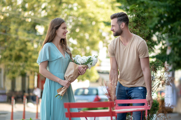 Bearded male pulling chair for cute young female with bouquet of flowers - Photo, Image