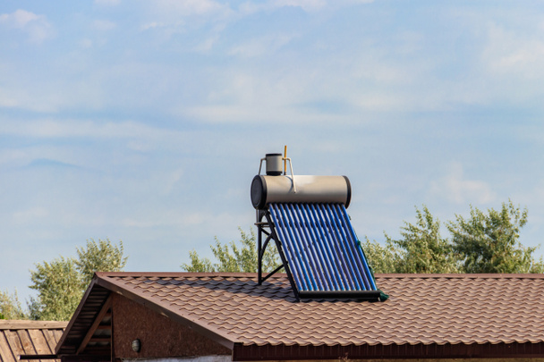 Napenergiával működő vízmelegítő egy lakóház tetején. Megújuló energia háztartás céljára - Fotó, kép