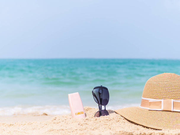 Güneş kremi şişesi, güneş gözlüğü, kumdaki mavi deniz şapkası. Güneş kavramından korumak için.. - Fotoğraf, Görsel
