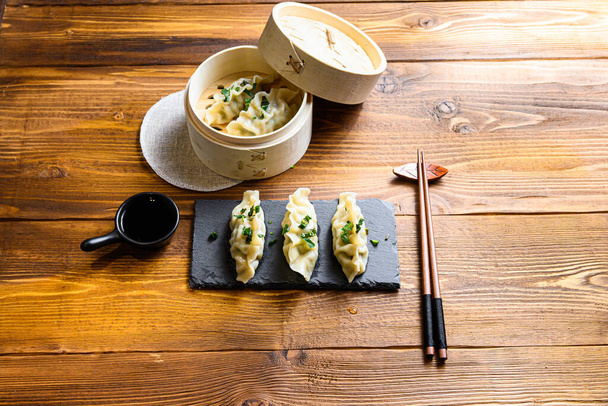 Fresh  vegetarian dumplings with wooden steamer on stone black slate. Chinese food on rustic old vintage wooden background. side view space for text. - 写真・画像
