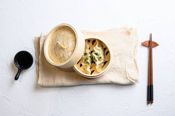 Bambuszgőzölő japán gyoza, gombóc snack, szójaszósszal és evőpálcikával tálalva fehér texturált kő asztali nézet. - Fotó, kép