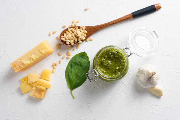 classic Basil pesto sauce in a glass jar. fresh basil leaves, grated parmesan cheese, pine nuts, garlic, white table concrete from above top view. - Fotoğraf, Görsel
