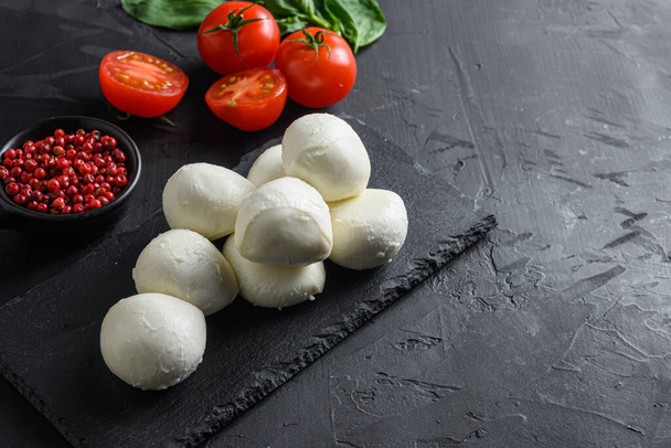 Fresh cherry tomatoes, basil leaf, mozzarella cheese on black slate stone chalkboard  Healthy Italian traditional caprese salad ingredients. Organic Mediterranean food concept,  selective focus space for text horizontal. - Photo, Image