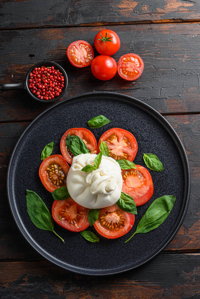 新鮮なトマトとバジルを添えた手作りのバラータチーズは、伝統的なイタリアのサラダ垂直方向のトップビューを残します。木のテーブル｜古い素朴な - 写真・画像