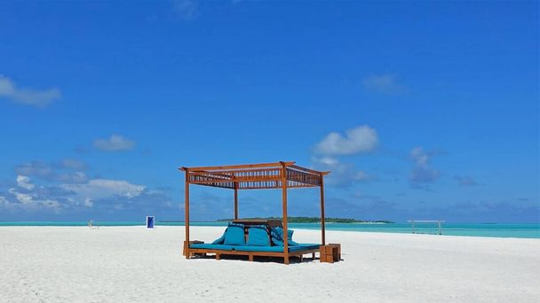 Détendez-vous sur la plage des Maldives. Il y a un auvent avec des sièges souples sur le sable blanc. L'océan marin est calme. Il y a de légers nuages dans le ciel azur. Pas de gens. Silence, bonheur. - Photo, image