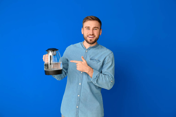 Young man with electric kettle on color background - Fotó, kép