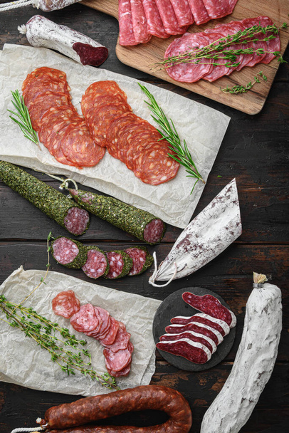 Variety of dry cured  chorizo, fuet and other sausages cut in slices with herbs on dark wooden background, topview. - Photo, Image