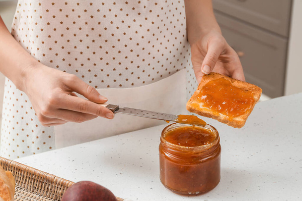 Γυναίκα εξάπλωση νόστιμο μαρμελάδα ροδάκινο σε ψωμί φέτα στην κουζίνα - Φωτογραφία, εικόνα