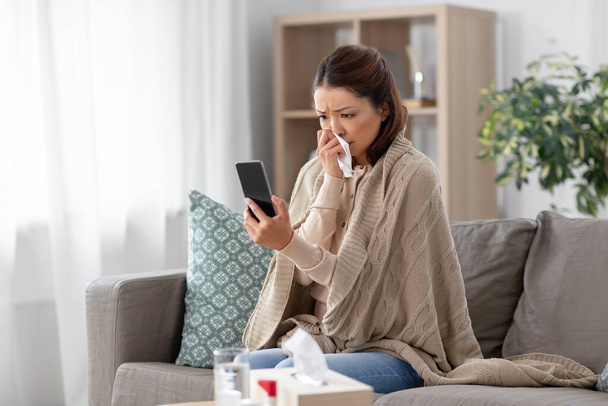 sick asian woman with smartphone at home - Fotó, kép