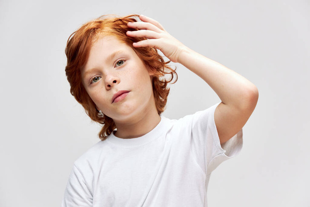 Kızıl saçlı çocuk kafasının yanında el ele tutuşmuş beyaz tişört giymiş.  - Fotoğraf, Görsel