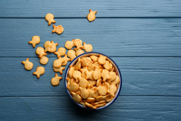 Delicious goldfish crackers in bowl on blue wooden table, flat lay - Fotó, kép