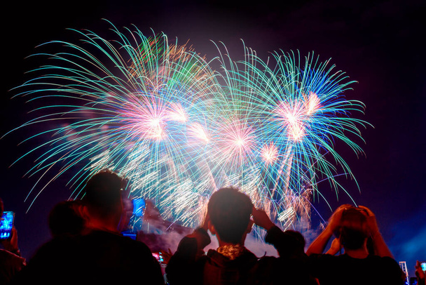 Tömeg tűzijátékot néz és ünnepli a város alapítását. Gyönyörű színes tűzijáték kijelző a városi ünneplés sötét éjszakai háttér. - Fotó, kép