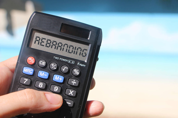 Rebranding on display of Calculator in hand sitting on summer beach. Marketing business concept. - Photo, Image