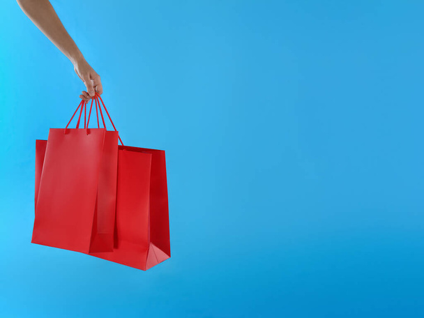Woman with paper shopping bags on light blue background, closeup. Space for text - Foto, imagen