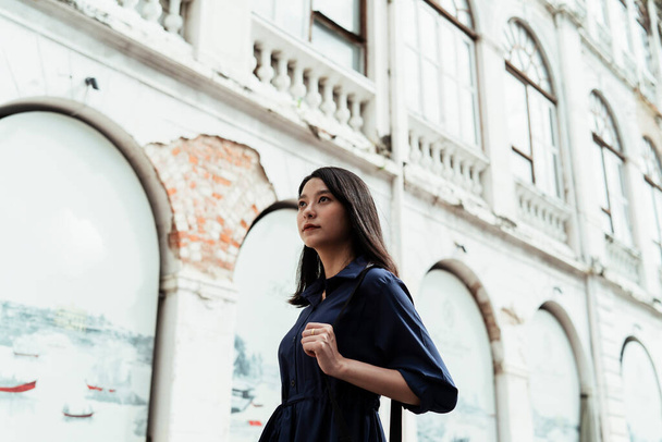 Schöne junge asiatische Frau auf blauem Kleid trägt schwarze Tasche zu Fuß auf der Straße am alten Architektur-Viertel. - Foto, Bild