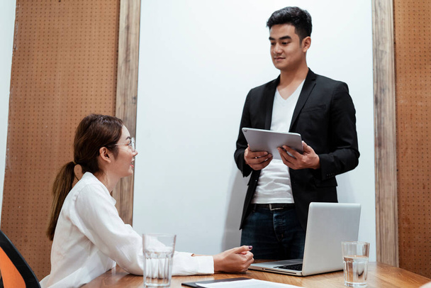Asian business boss on black suit standing holding tablet doing job interview with asian young lady applicant sitting on table. - Φωτογραφία, εικόνα