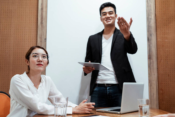 Asijské obchodní šéf v černém obleku držení notebook ukazuje prezentaci na obrazovce ukázat, jak společnost pracuje s mladou asijskou dámu na bílém tričku nosí brýle sedí v místnosti. - Fotografie, Obrázek