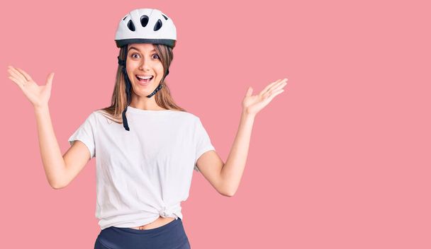 Mladá krásná dívka na sobě cyklistické helmy slaví vítězství se šťastným úsměvem a vítězným výrazem se zdviženýma rukama  - Fotografie, Obrázek