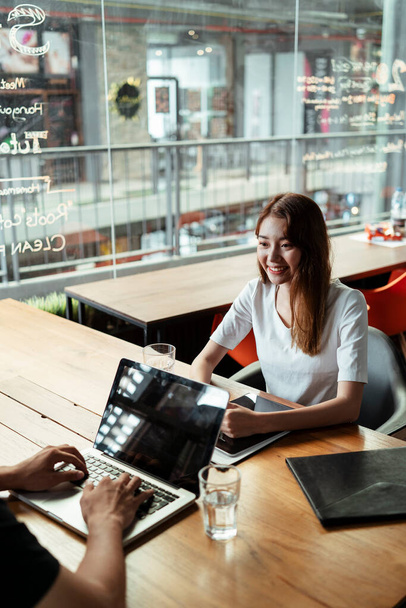 Junge asiatische Mädchen haben ein Treffen mit Kunden im Café in der Stadt. Mädchen führt ein Interview im Freien im Café mit Geschäftsinhaber. - Foto, Bild