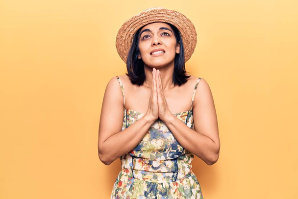 Young beautiful latin woman wearing summer hat begging and praying with hands together with hope expression on face very emotional and worried. begging.  - Foto, imagen
