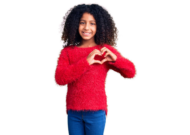 Niño afroamericano con el pelo rizado usando suéter casual de invierno sonriendo en el amor mostrando el símbolo del corazón y la forma con las manos. concepto romántico.  - Foto, Imagen