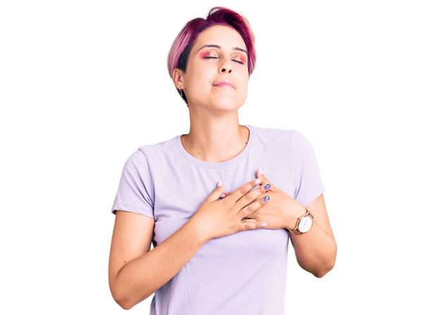 Young beautiful woman with pink hair wearing casual clothes smiling with hands on chest with closed eyes and grateful gesture on face. health concept.  - Photo, Image