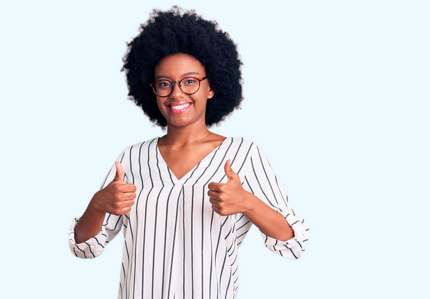 Mujer afroamericana joven con ropa casual y gafas signo de éxito haciendo gesto positivo con la mano, pulgares arriba sonriendo y feliz. expresión alegre y gesto ganador.  - Foto, Imagen