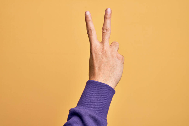 Рука кавказького молодого чоловіка, що показує пальці над ізольованим жовтим тлом, підраховує номер 2 з двома пальцями, жестикулює перемогу і символ переможця
 - Фото, зображення