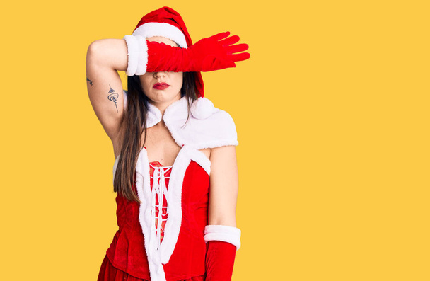 Genç beyaz kadın Noel Baba kostümü giyip gözlerini kollarıyla kapatıyor, ciddi ve üzgün görünüyor. Görme, saklama ve reddetme konsepti  - Fotoğraf, Görsel