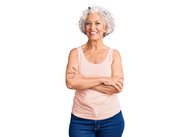 Eine ältere grauhaarige Frau in lässiger Kleidung lächelt glücklich mit verschränkten Armen in die Kamera. positive person.  - Foto, Bild