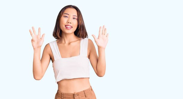 Young beautiful chinese girl wearing casual clothes showing and pointing up with fingers number nine while smiling confident and happy.  - Фото, изображение
