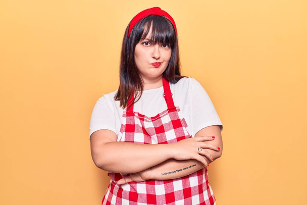 Young plus size woman wearing apron skeptic and nervous, disapproving expression on face with crossed arms. negative person.  - Photo, Image