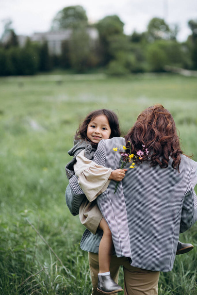 Πορτρέτο της hipster μητέρα με την κόρη στην αγκαλιά της στο πεδίο. Η οικογένεια περνάει καλά μαζί. - Φωτογραφία, εικόνα