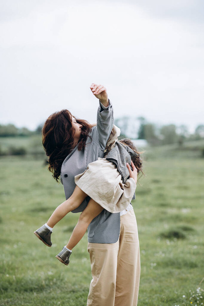 Portrait of hipster mother with daughter in her arms in the field. The family is having fun together - Fotoğraf, Görsel