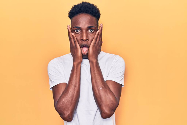 Young african american man wearing casual clothes afraid and shocked, surprise and amazed expression with hands on face  - Photo, Image
