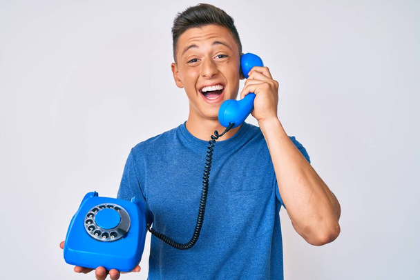 Fiatal spanyol fiú kezében vintage telefon mosolyogva és nevetve hangosan, mert vicces őrült vicc.  - Fotó, kép