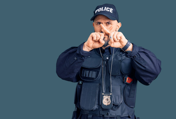 Nuori komea mies yllään poliisi yhtenäinen hylkääminen ilme ristikkäin sormet tekee negatiivinen merkki  - Valokuva, kuva