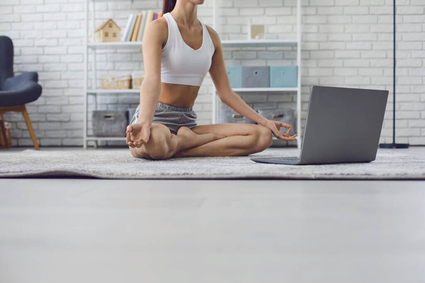 Ausgeschnittene Ansicht einer jungen Frau, die in der Nähe ihres Laptops zu Hause meditiert. Yogalehrer gibt Online-Kurs in Innenräumen - Foto, Bild