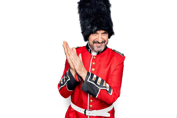Středního věku hezký wales stráž muž nosí tradiční uniformu přes bílé pozadí tleskání a tleskání šťastný a radostný, usmívající se hrdé ruce dohromady - Fotografie, Obrázek