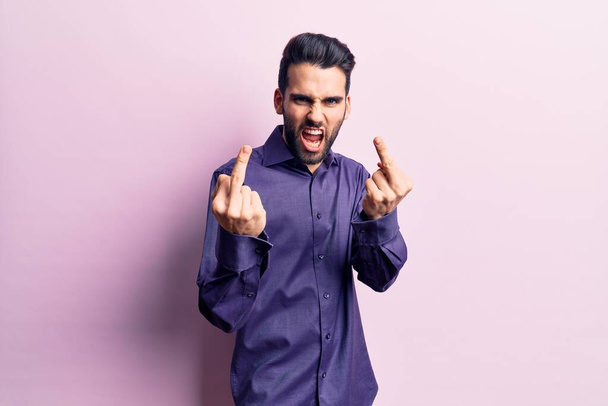 Young handsome man with beard wearing casual shirt showing middle finger doing fuck you bad expression, provocation and rude attitude. screaming excited  - Fotoğraf, Görsel