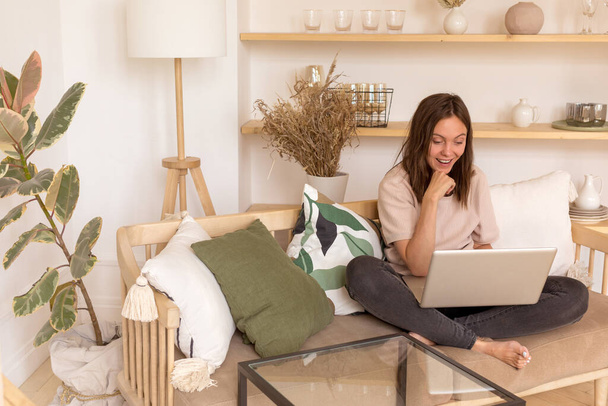 Iloinen nainen käyttää kannettavaa tietokonetta sohvalla - Valokuva, kuva