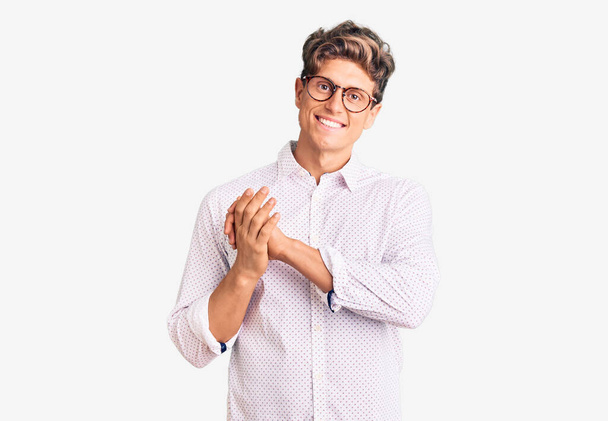 Young handsome man wearing business clothes and glasses clapping and applauding happy and joyful, smiling proud hands together  - Photo, Image