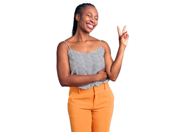 Mujer afroamericana joven vistiendo ropa casual sonriendo con la cara feliz guiñando el ojo a la cámara haciendo señal de victoria. número dos.  - Foto, Imagen