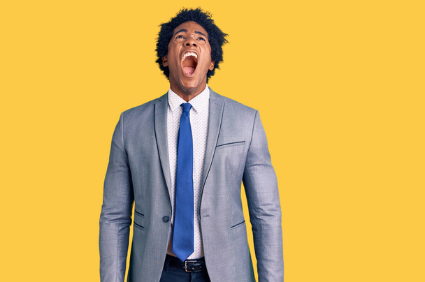 Hombre afroamericano guapo con pelo afro vistiendo chaqueta de negocios enojado y loco gritando frustrado y furioso, gritando con ira. rabia y concepto agresivo.  - Foto, imagen