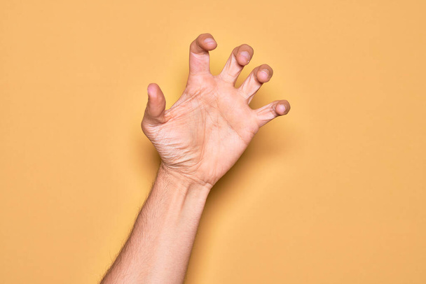 Рука кавказького молодого чоловіка, що показує пальці над ізольованим жовтим тлом, захоплює агресивний і лякає пальцями, насильством і розчаруванням
 - Фото, зображення