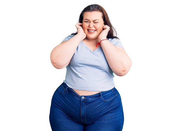 Young plus size woman wearing casual clothes covering ears with fingers with annoyed expression for the noise of loud music. deaf concept.  - Foto, Imagen