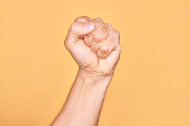 Mano de joven caucásico mostrando los dedos sobre fondo amarillo aislado haciendo protesta y gesto de revolución, puño expresando fuerza y poder - Foto, Imagen