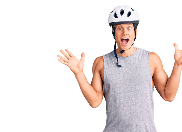 Bisiklet kaskı takan genç yakışıklı adam çılgın ve başarıyı kollarını kaldırıp heyecanla haykırarak kutluyor. Kazanan konsept  - Fotoğraf, Görsel