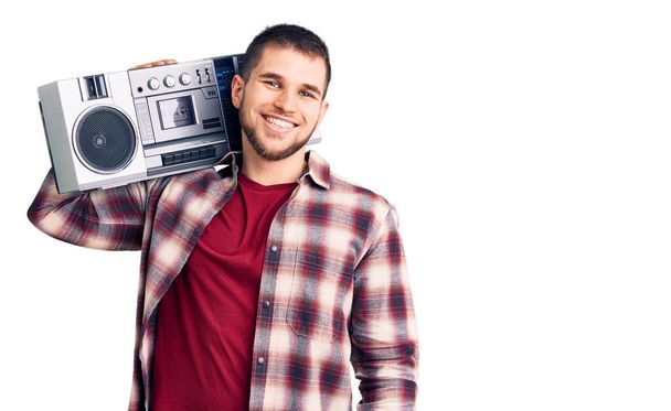 Mladý pohledný muž poslouchá hudbu drží boombox vypadá pozitivně a šťastně stojící a usmívá se s sebevědomým úsměvem ukazuje zuby  - Fotografie, Obrázek
