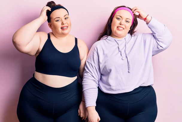 Young plus size twins wearing sportswear confuse and wonder about question. uncertain with doubt, thinking with hand on head. pensive concept.  - Photo, Image